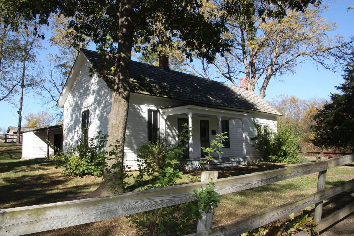 The white farmhouse at the Jesse James Birthplace behind a split-rail fence